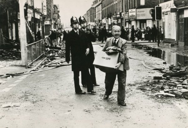 A shopkeeper carries away his goods in a box after shops were looted during the Toxteth Riots